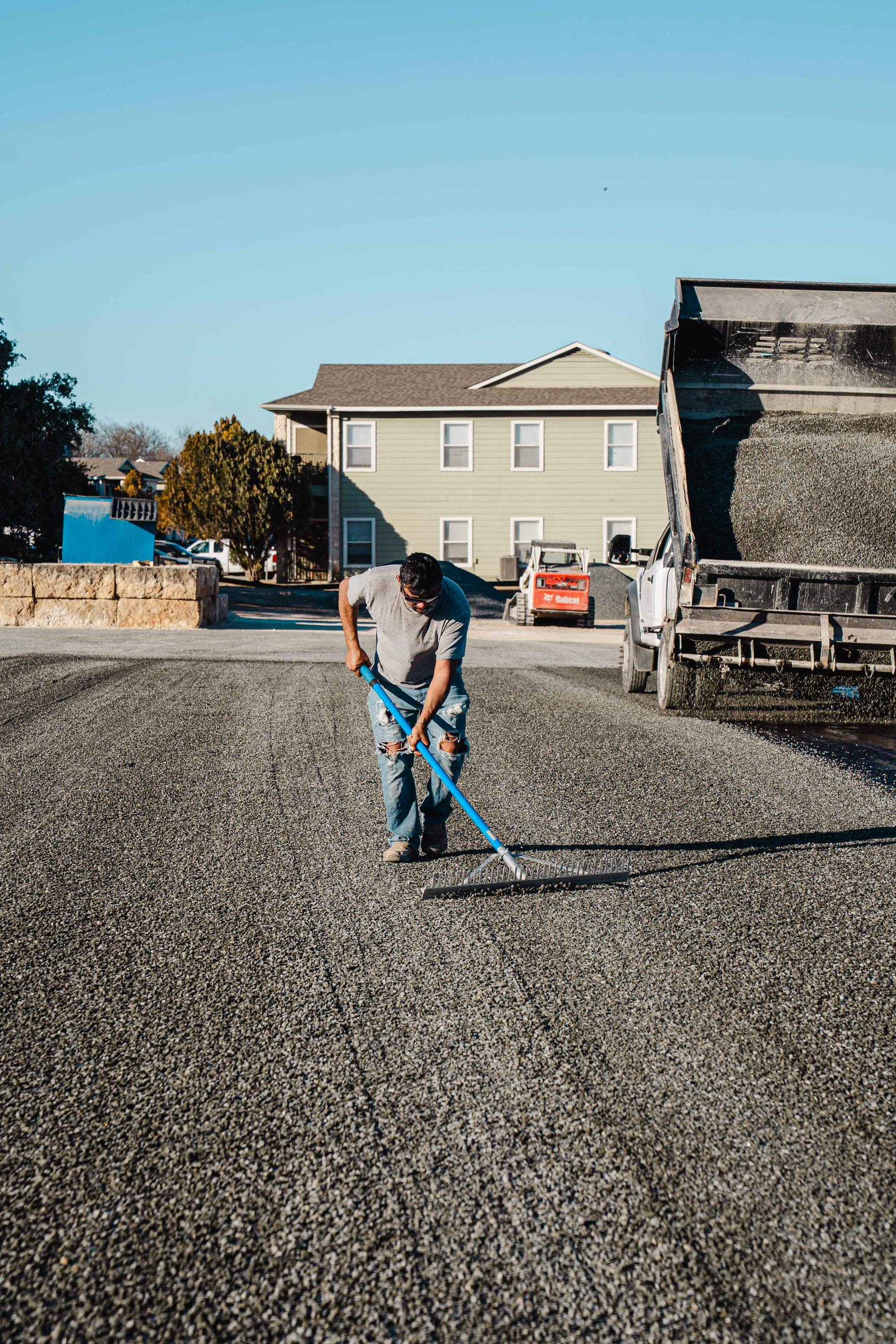 Worker raking loose aggregate across a newly surfaced area