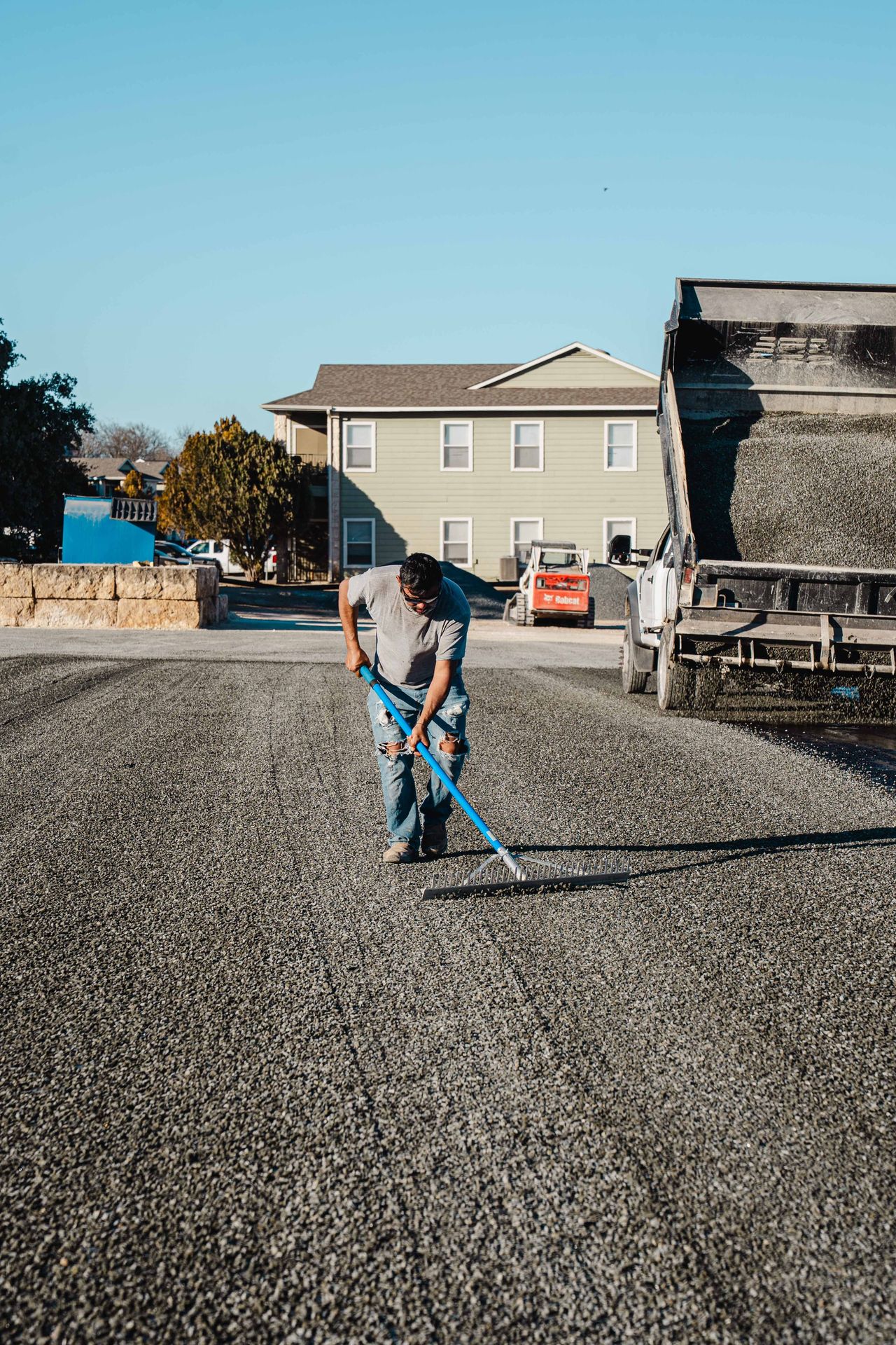 Worker raking loose aggregate across a newly surfaced area
