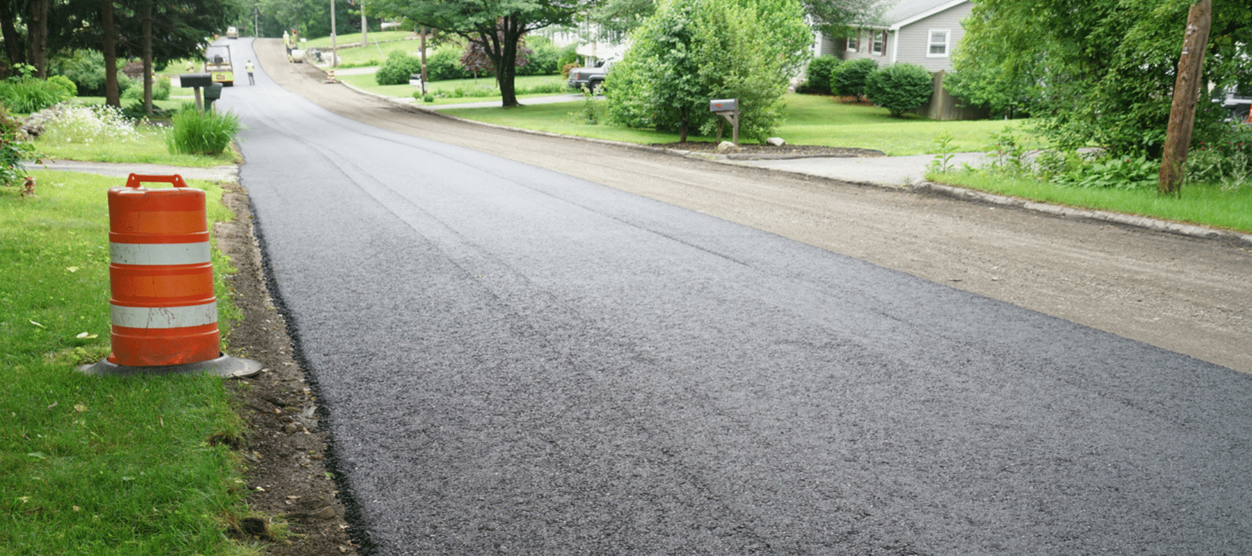 A newly paved residential road with an orange construction barrel in the foreground