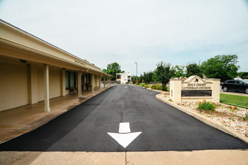 A newly paved asphalt driveway with white directional arrow marking leading to Holy Ghost Lutheran Church entrance.