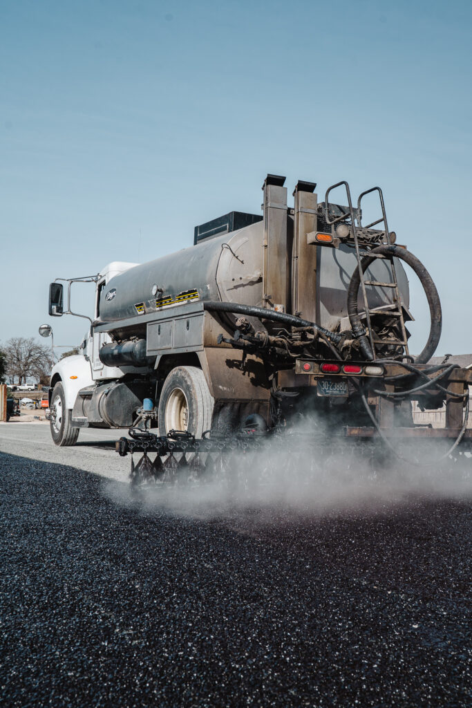 Alligatoring pavement pattern on HOA road in Willow City, TX: a tanker truck spraying liquid asphalt distributor onto