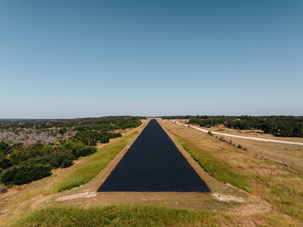 Asphalt drainage pooling causing premature wear in Center Point TX: a newly paved asphalt road stretching straight across