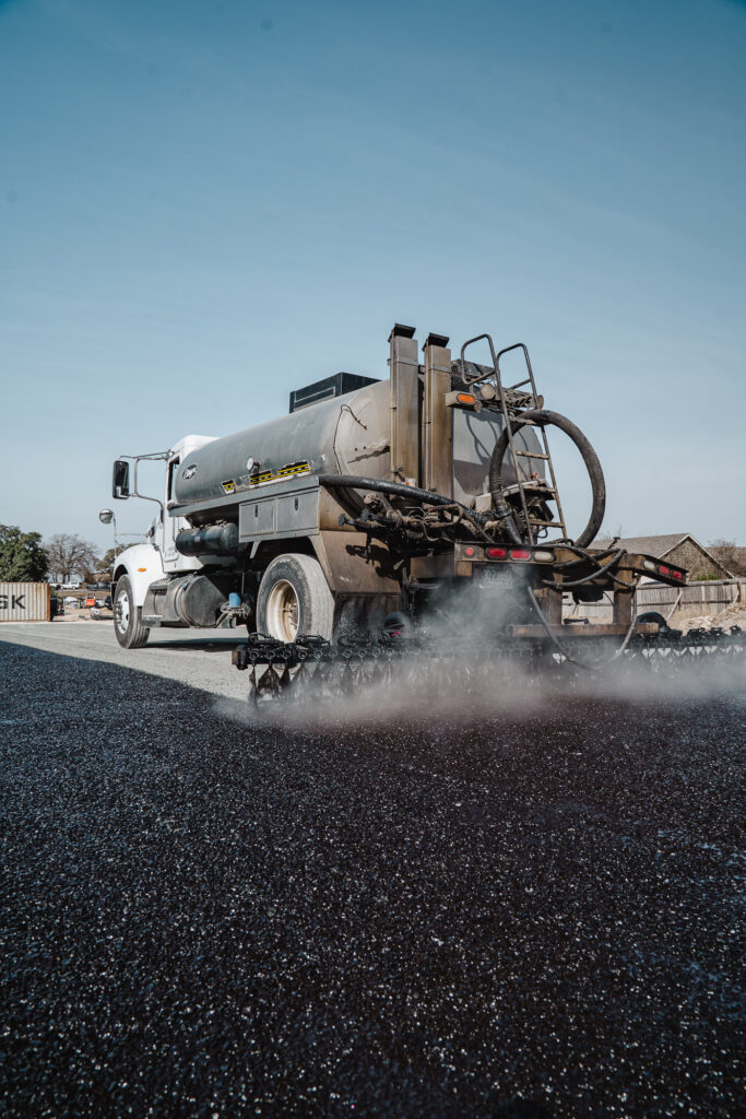 Asphalt paving surface flushing and bleeding in Bergheim TX: a vacuum truck actively spraying liquid asphalt sealant onto