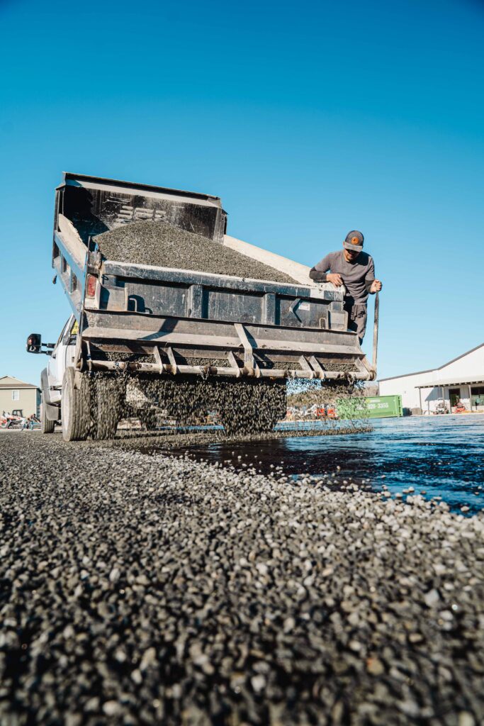 Asphalt raveling exposing aggregate on parking lot surface in Bandera TX: a dump truck unloading gravel and aggregate