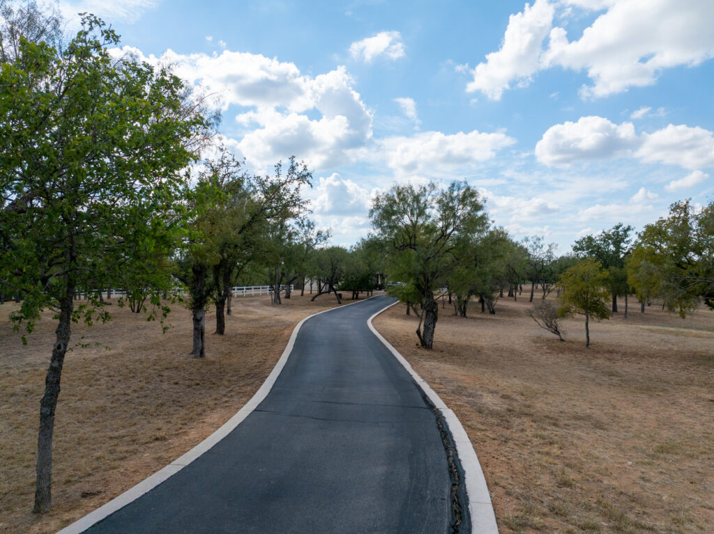 Bleeding asphalt seeping through seal coat in Boerne TX: a newly paved curved asphalt path with white edge lines running