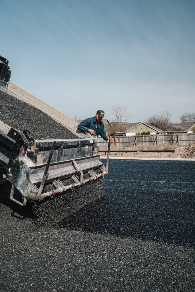 A dump truck actively spreading hot asphalt material onto a residential driveway during a paving project.