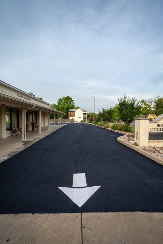 Driveway paving sinking at storm drain outlet in Fair Oaks Ranch, TX: a newly paved asphalt driveway with white directional