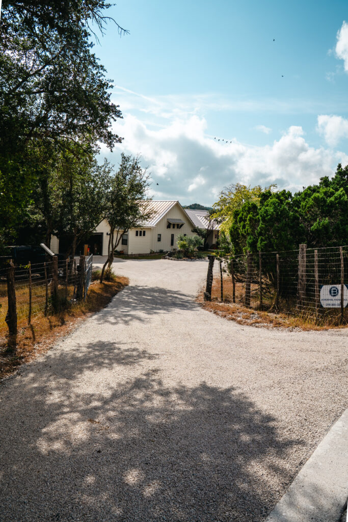 Edge crumbling on private driveway entrance in Doss, TX: a freshly paved gravel driveway leading to a modern white farmhouse