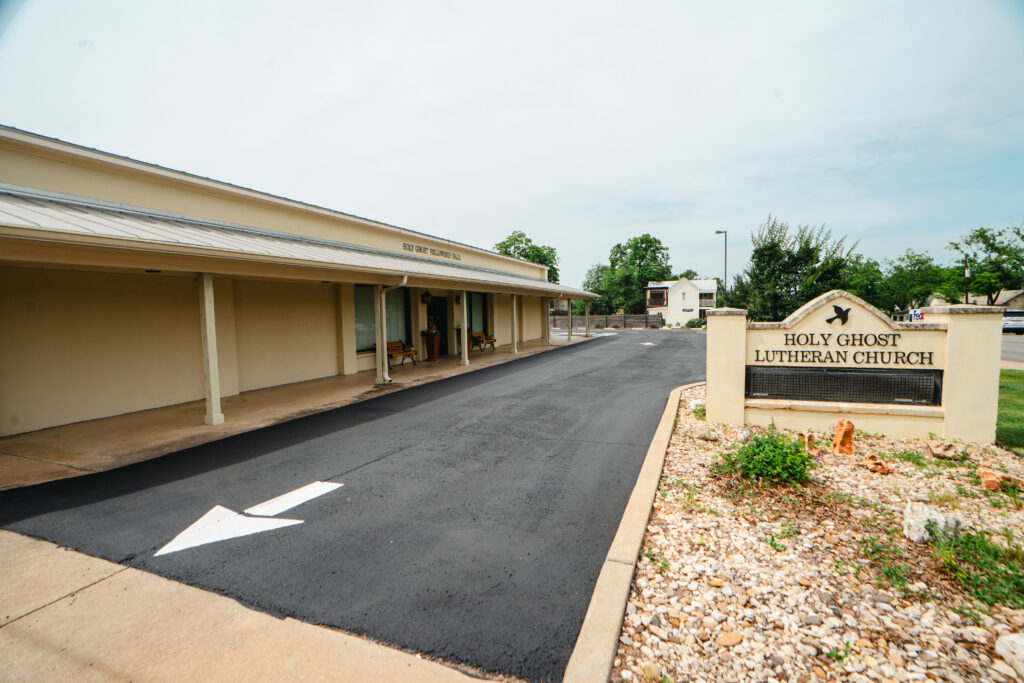 Oxidized asphalt losing color in Stonewall TX: a freshly paved asphalt parking lot in front of Holy Ghost Lutheran Church