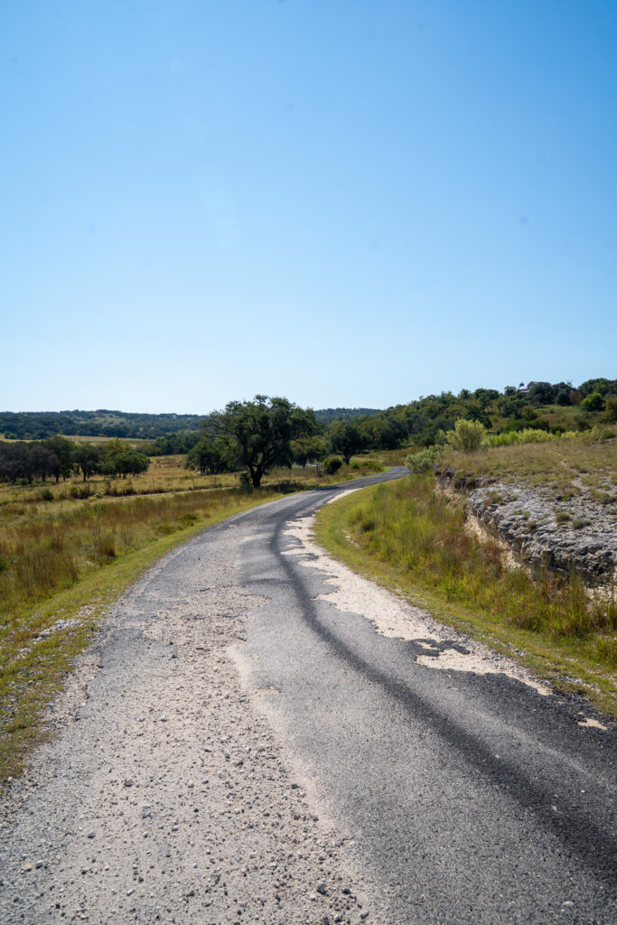 Seal coat adhesion failure on ranch road in Hunt TX: a winding asphalt paved road through rural Texas Hill Country landscape