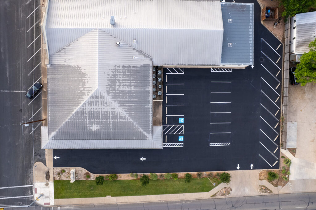 Soft asphalt spots in summer heat in Boerne, TX: aerial view of a freshly paved and newly striped asphalt parking lot